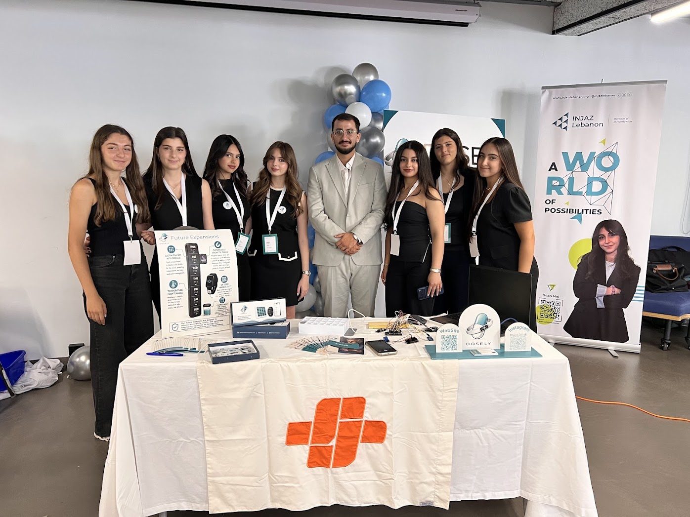 Rami Kronbi standing with the Dosely team at their booth, a table with their pillbox and bracelet prototypes, at the INJAZ Lebanon exhibition.