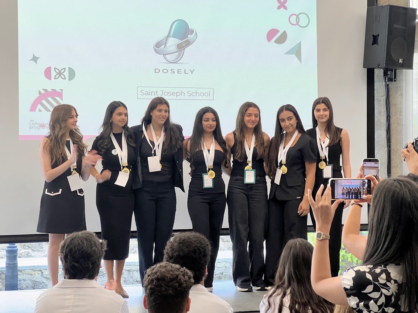 The Dosely team from Saint Joseph School on stage at the INJAZ Lebanon final, wearing medals, in front of a screen showing their logo.