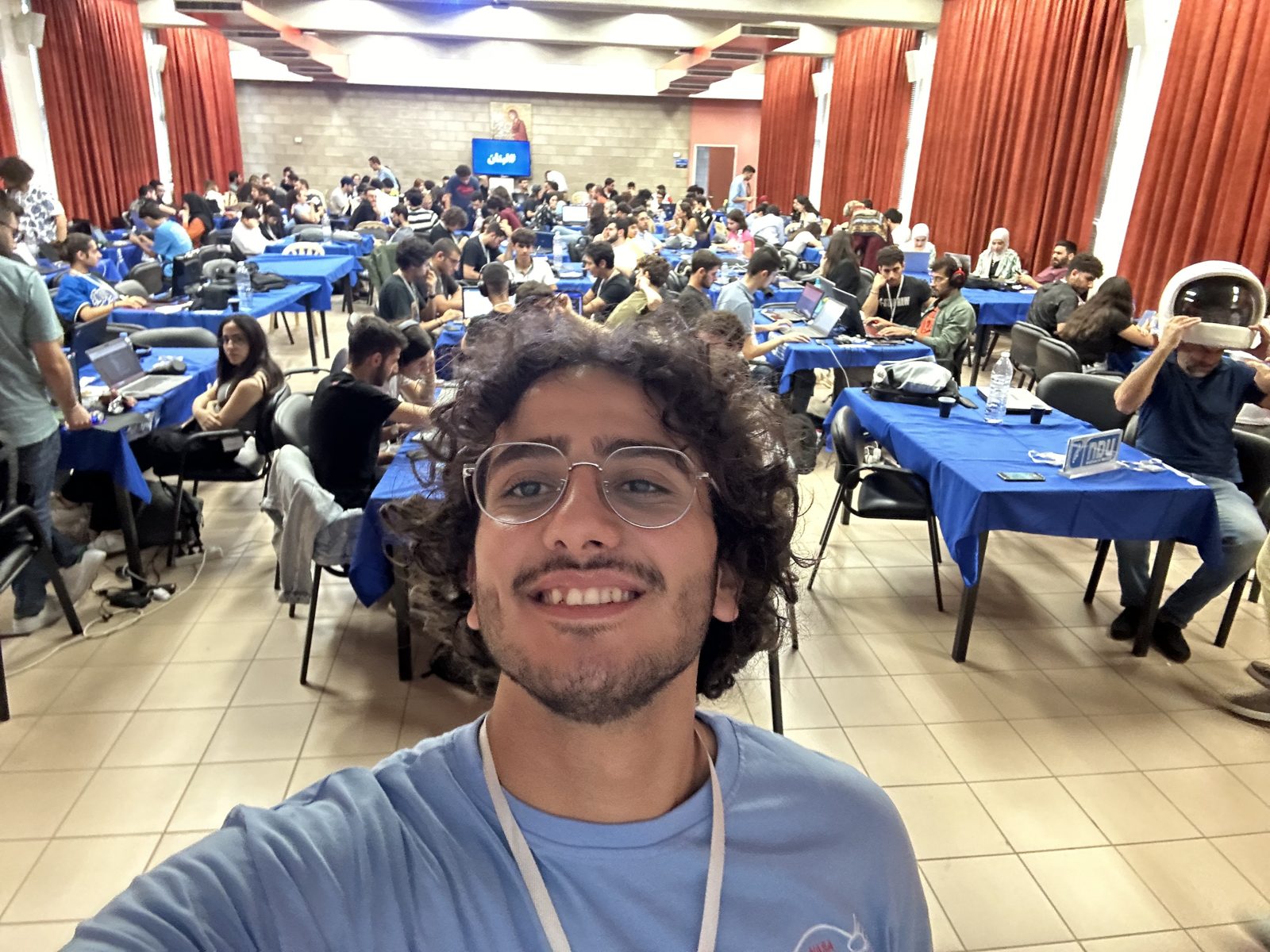 Rami Kronbi taking a selfie in front of a hall full of teams working at laptops during NASA Space Apps Beirut.